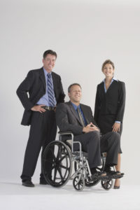 three business people posing for a photo. One person is in a wheelchair.