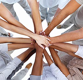 a group of cooworkers put ll their hands into the center as a show of teamwork